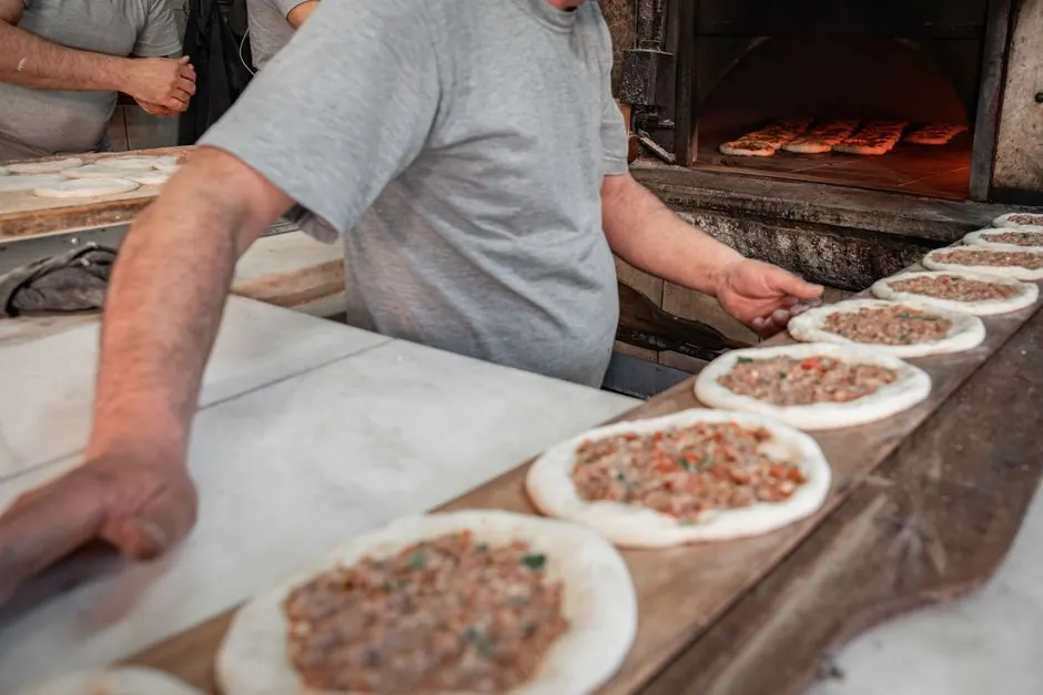 Chef preparing traditional Middle Eastern flatbreads with minced meat in a stone oven.